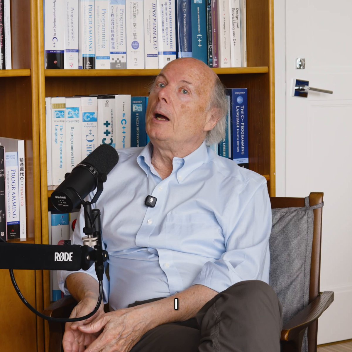 Bjarne Stroustrup 인터뷰 장면 — 다국어 C++ 책 가득한 책장 앞, RØDE 마이크 앞에서 본인이 직접 발언
